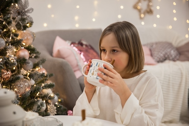 Dziewczyna pije kawę z pianką marshmallow w świątecznym salonie