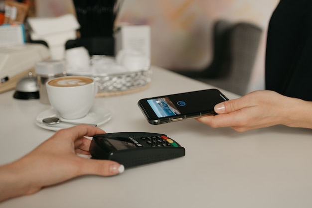 Dziewczyna płacąca smartfonem za pomocą zbliżeniowej technologii NFC w kawiarni