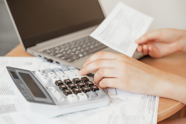 Zdjęcie dziewczyna płaci rachunki za media w internecie ręce kobiet liczą na kalkulatorze, księgowy pracuje z dokumentami kobiece ręce trzymają paragon i pracują z laptopem i kalkulatorem