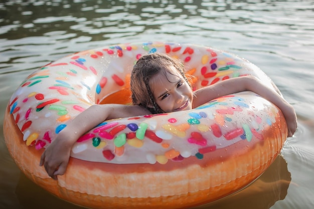 Dziewczyna pływa z dużym nadmuchiwanym pierścieniem w kształcie pączka nad jeziorem w upalny letni dzień, happy summertime cottagecore