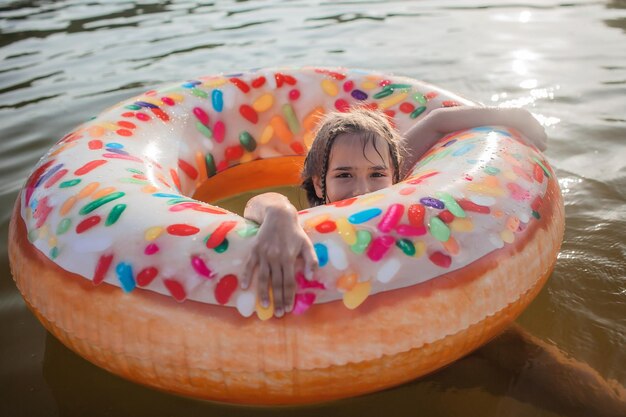 Dziewczyna pływa z dużym nadmuchiwanym pierścieniem w kształcie pączka nad jeziorem w upalny letni dzień, happy summertime cottagecore