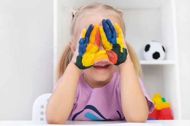 Dziewczyna pokazuje malowane ręce. Ręce malowane kolorowymi farbami. Oczy zamknięte dłońmi