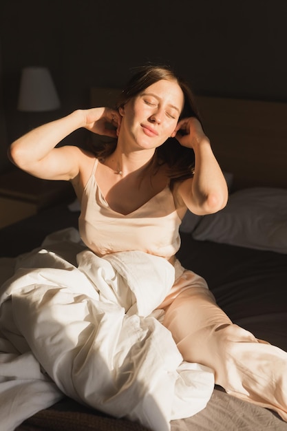 Dziewczyna portret budzi się rano rozciąga się w łóżku i słońce świeci z okna szczęśliwa młoda kobieta