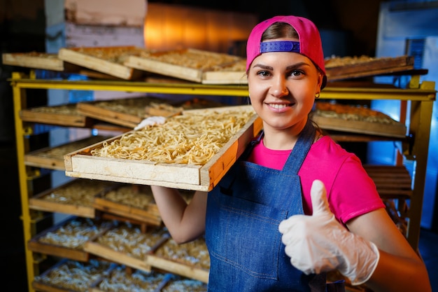 Dziewczyna Pracuje Przy Produkcji Spaghetti. Robienie Makaronu. Fabryka Makaronów. Produkcja Etapowa Makaronów. Surowy Makaron. Pracownik Z Pudełkiem Makaronu.