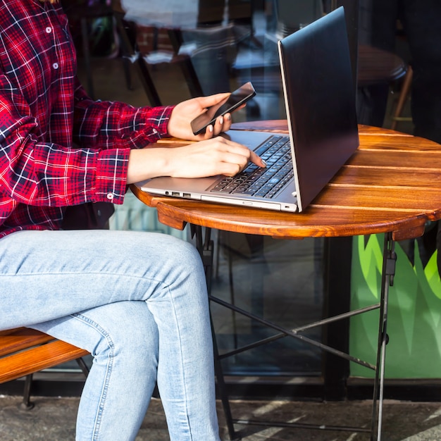 Dziewczyna pracuje za laptopem przy stoliku w kawiarni obok filiżanki kawy