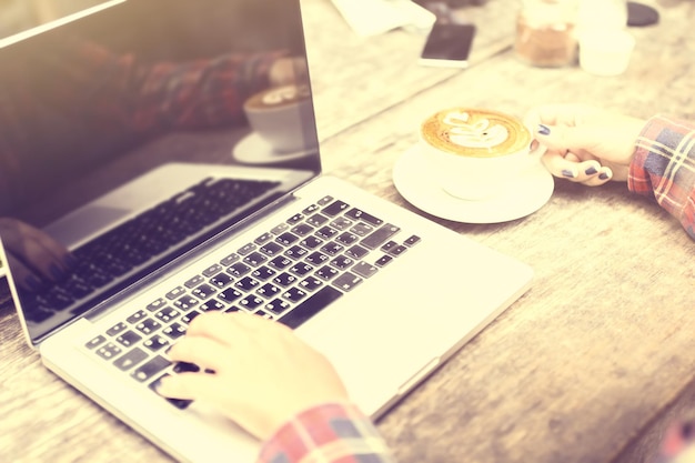 Dziewczyna ręce z laptopem i cappuccino na drewnianym stole efekt vintage