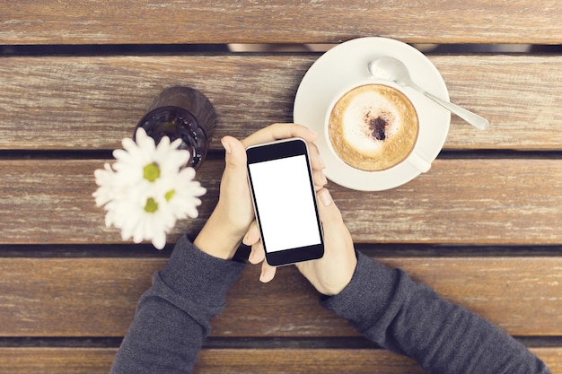 Dziewczyna ręce z pustym smartphone filiżanką kawy i kwiatów na drewnianym stole