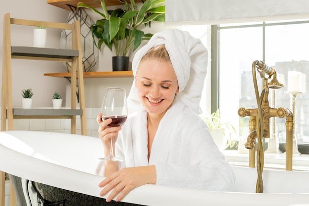 dziewczyna relaksuje się w łazience przy lampce wina, kobieta odpoczywa szczęśliwa w białej frotowej szacie