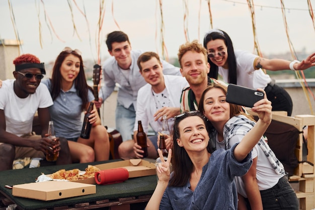 Dziewczyna robi selfie Z pyszną pizzą Grupa młodych ludzi w zwykłych ubraniach urządza razem imprezę na dachu w ciągu dnia