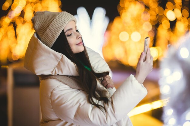 Dziewczyna robi sobie zdjęcia telefonem w zimowym mieście na tle bokeh