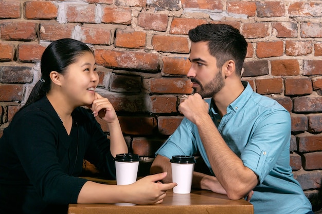 Dziewczyna rozmawia o czymś z młodym mężczyzną, gdy siedzą przy stoliku w kawiarni na tle szorstkiego ceglanego muru