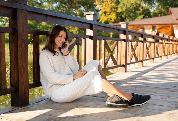 Dziewczyna rozmawia przez telefon siedząc na ulicy na drewnianym moście Piękny słoneczny jesienny dzień