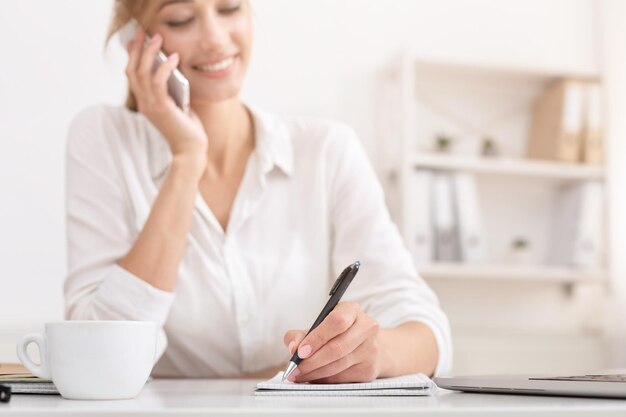 Dziewczyna rozmawiająca przez telefon komórkowy, robiąca notatki w miejscu pracy