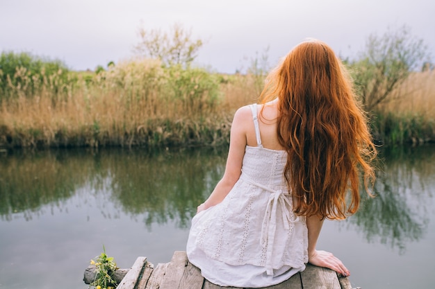 dziewczyna siedzi na drewnianym molo nad rzeką lub jeziorem