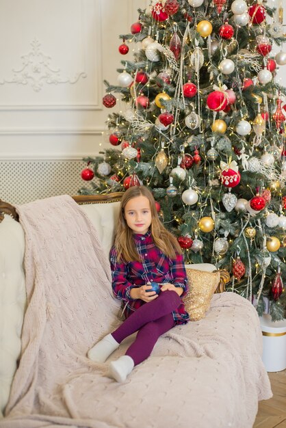 dziewczyna siedzi na kanapie w Boże Narodzenie na tle choinki w domu
