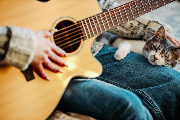 Dziewczyna siedzi na kanapie w pokoju i gra na gitarze dla kota Przyjaźń i miłość do zwierzaka