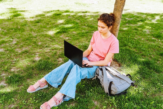 Dziewczyna siedzi na trawie i pracuje na laptopie.