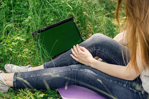 Dziewczyna siedzi na trawie i pracuje przy laptopie samokształcenie na odległość koncepcja nauki na odległość w plenerze