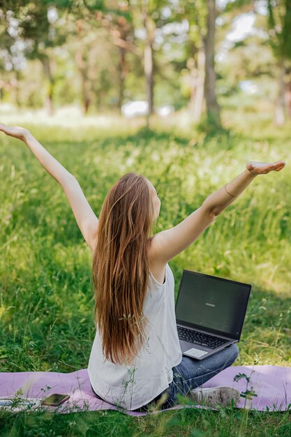 Dziewczyna siedzi na zewnątrz i pracuje przy laptopie cieszy się pod koniec dnia pracy samokształcenie na własny rachunek koncepcja nauki zdalnej i pracy na świeżym powietrzu