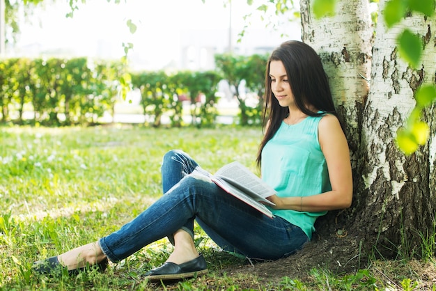 Dziewczyna siedzi w trawie czytając książkę latem