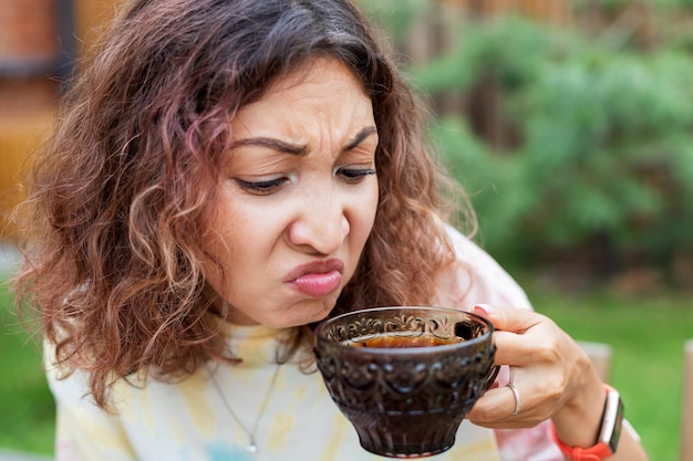 Zdjęcie dziewczyna smakuje gorzką i mocną herbatę puerh lub kawę i robi niezadowoloną minę