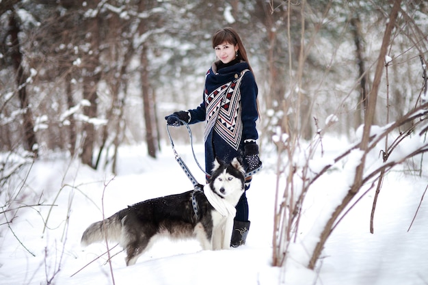 Dziewczyna spaceruje z psem husky syberyjski w śnieżnym lesie zimą.