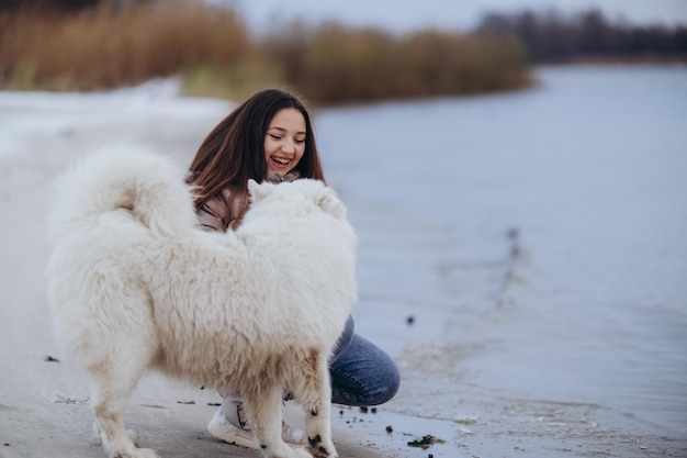 Zdjęcie dziewczyna spaceruje ze swoim ukochanym zwierzęciem samojedem zimą na brzegu jeziora w parku spacerując z psem zimą