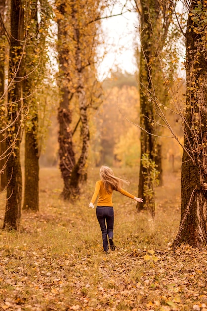 Dziewczyna spacery w lesie jesienią. Młoda kobieta kręci się na tle drzew pomarańczowych..