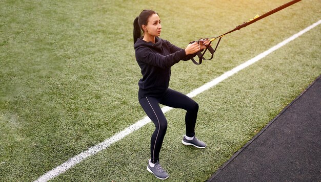 Dziewczyna sportowca trenująca za pomocą trx na boisku sportowym mieszana rasa młoda dorosła kobieta ćwiczy z