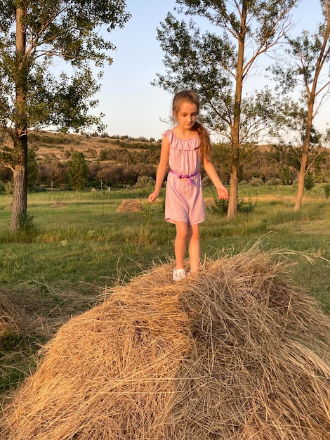 Dziewczyna stoi na beli siana w polu.