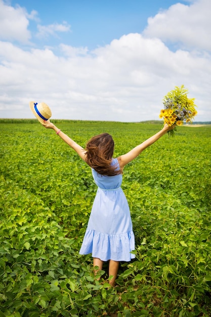 Dziewczyna stoi na polu z bukietem żółtych kwiatów i słomkowym kapeluszem