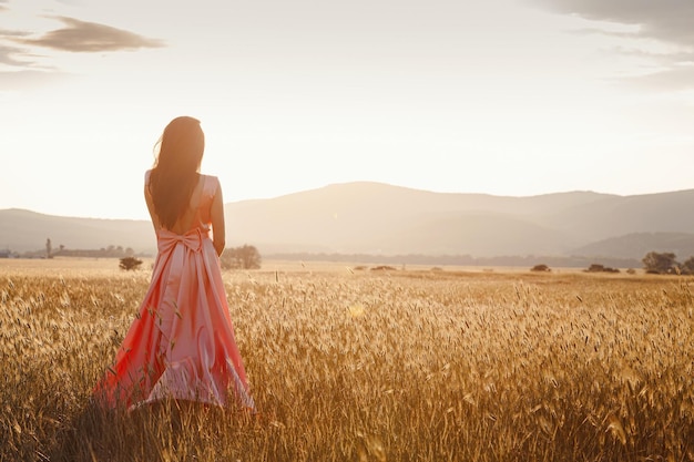 Dziewczyna tańczy na polu w pięknej różowej sukience o zachodzie słońca