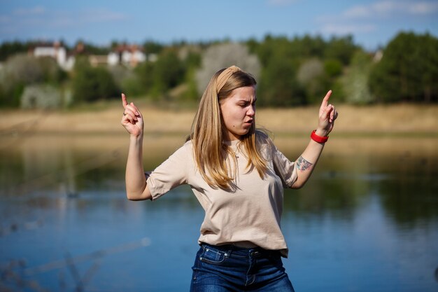 Dziewczyna tańczy w pobliżu jeziora, słoneczna pogoda. Młoda kobieta raduje się życiem, tańczy i śpiewa. Ma dobry nastrój i uśmiech na twarzy.