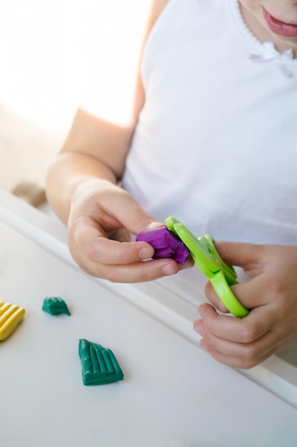 Dziewczyna Toddler trzyma jedną ręką zielone nożyczki do zabawek, a drugą plastelinę Forma w kształcie