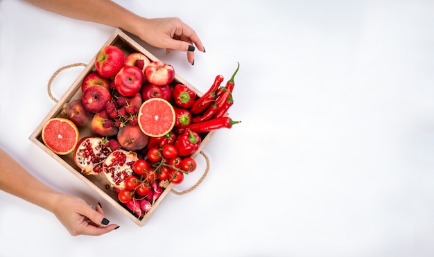 Dziewczyna trzyma drewnianą tacę z świeżymi czerwonymi warzywami i owoc na szarym tle. Zdrowe jedzenie koncepcja wegetariańska.