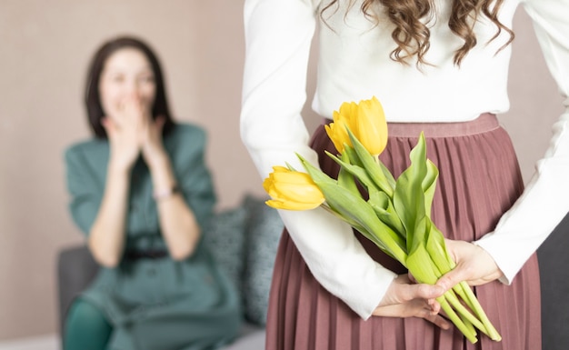 Dziewczyna trzyma kwiaty dla matki za plecami, zbliżenie