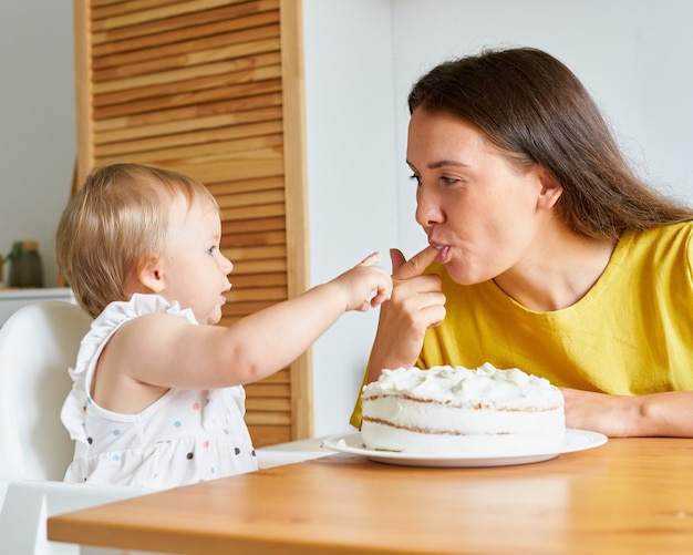 Dziewczyna trzyma palec matce próbując kremu z ciasta matka uśmiecha się i liże palec