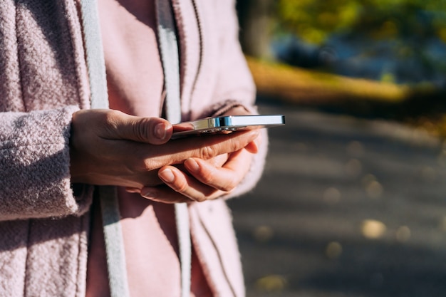 Dziewczyna trzyma w dłoniach nowoczesny smartfon, będąc na ulicy jesienią.