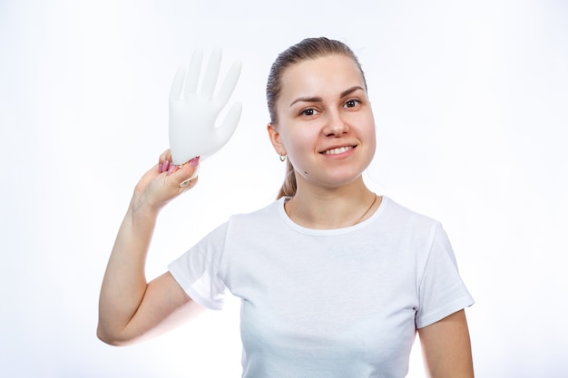 Dziewczyna trzyma w rękach białe rękawiczki medyczne. Ochrona przed zarazkami i wirusami. Jest w białej koszulce na białym tle.