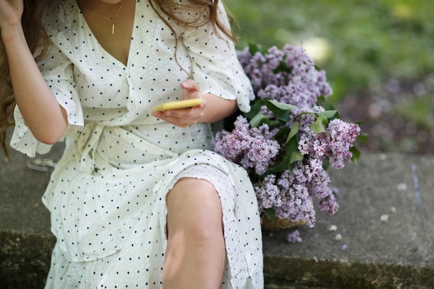 Dziewczyna Trzyma W Rękach Wiklinowy Kosz Z Kwiatami. Kosz Z Bzami. Dziewczyna I Kwiaty. Spacer Z Koszem Bzu W Rękach. Florystyka. Przytulna Atmosfera Ze świeżymi, Pachnącymi Kwiatami.