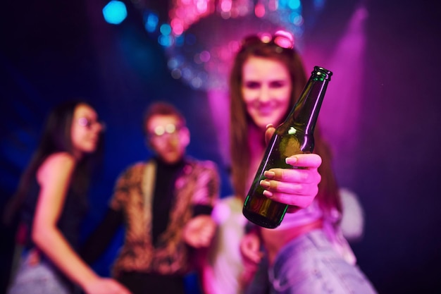 Dziewczyna trzymająca butelkę Młodzi ludzie bawią się w nocnym klubie z kolorowymi światłami laserowymi