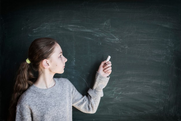 Zdjęcie dziewczyna trzymająca kredę, stojąca na tablicy w klasie
