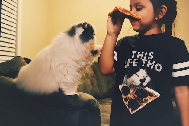 Dziewczyna trzymająca pizzę, stojąca obok kota w domu