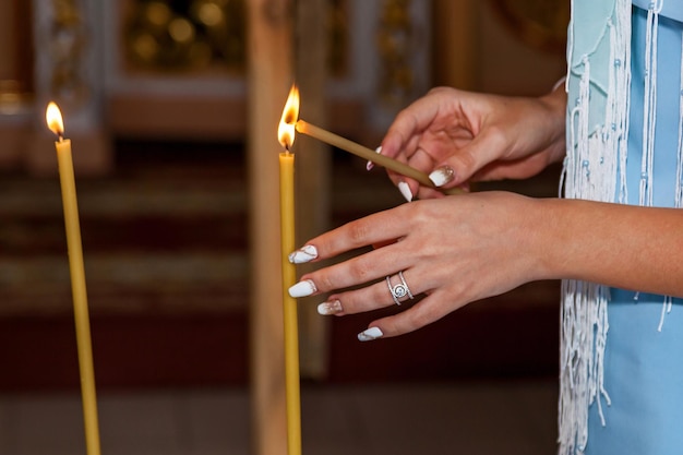 Zdjęcie dziewczyna trzymająca świece woskowe. żółta świeca zapaliła ogień na cześć. palenie świec woskowych w kościele