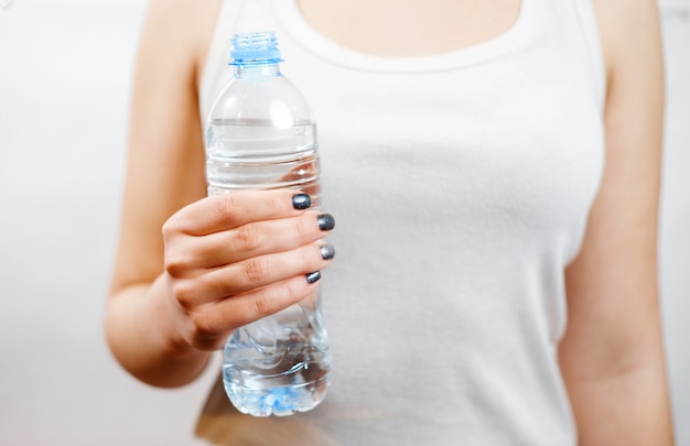 Dziewczyna trzymająca w dłoni butelkę wody, nie widzi twarzy, mała butelka, Biała koszula, zbliżenie