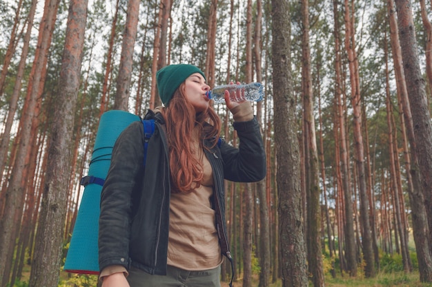 Dziewczyna turysta korzystających z wody. Szczęśliwa kobieta turysta z plecakiem wody pitnej z butelki w przyrodzie.