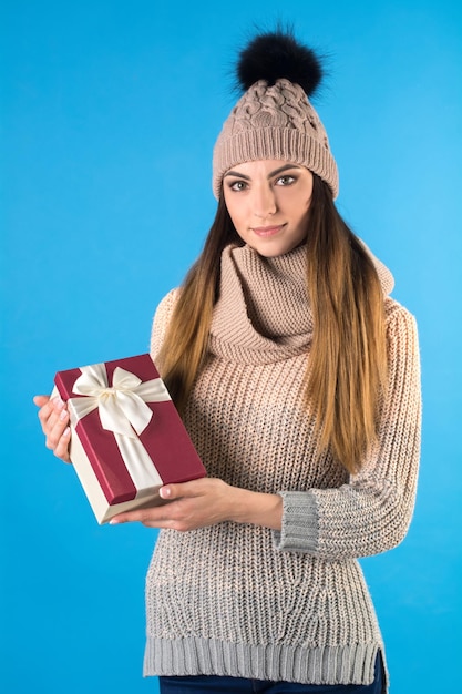 Dziewczyna ubrana jest w ciepły sweter z dzianiny i czapkę z pudełkiem prezentowym