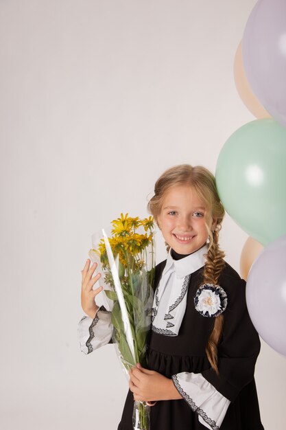 Dziewczyna uczennica, uczennica pierwszej klasy w mundurku szkolnym na białym tle z kulkami i kwiatami