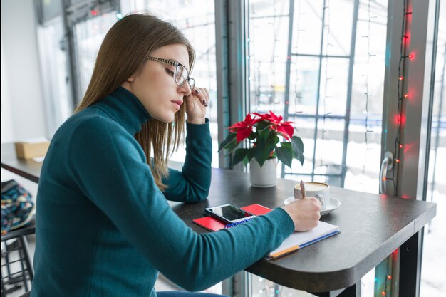 Dziewczyna ucznia studiowanie w kawiarni używać smartphone i notatnika