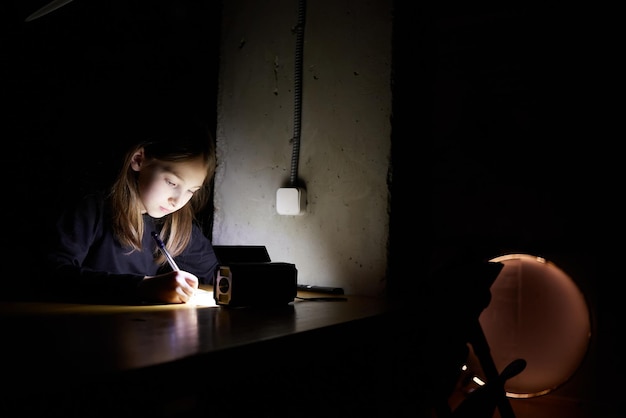Dziewczyna uczy się po ciemku Dziecko odrabia lekcje, gdy w domu nie ma prądu